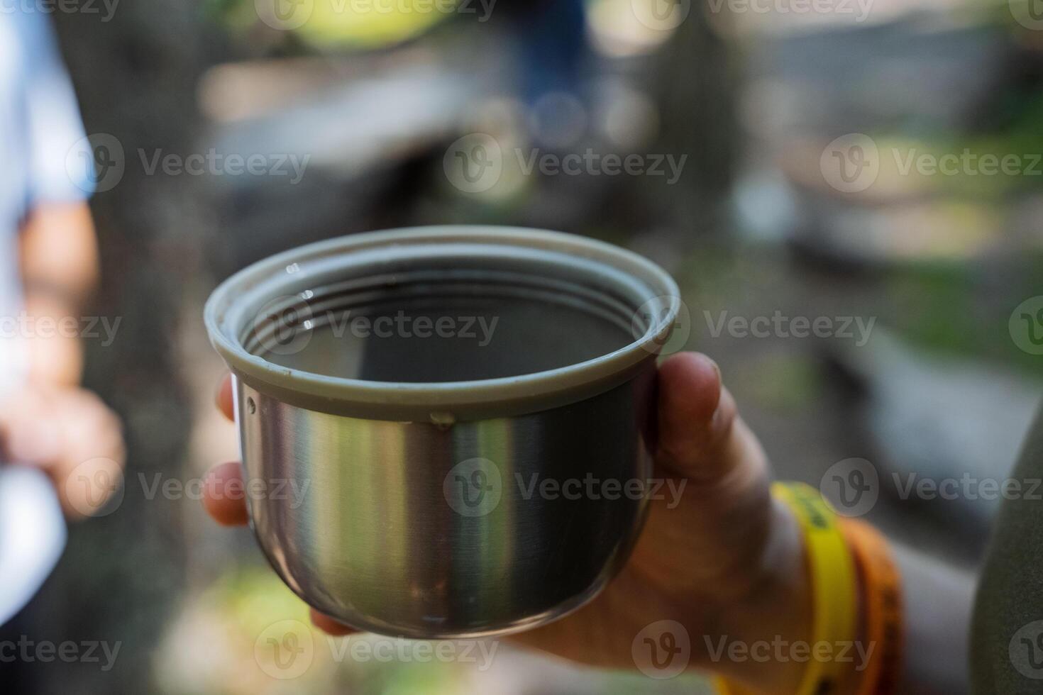 A cup of delicious teana to nature, a person holds a mug from a thermos with a hot naptka, a tourist drinks coffee in nature, a thermal glass, a hike in the mountains. photo