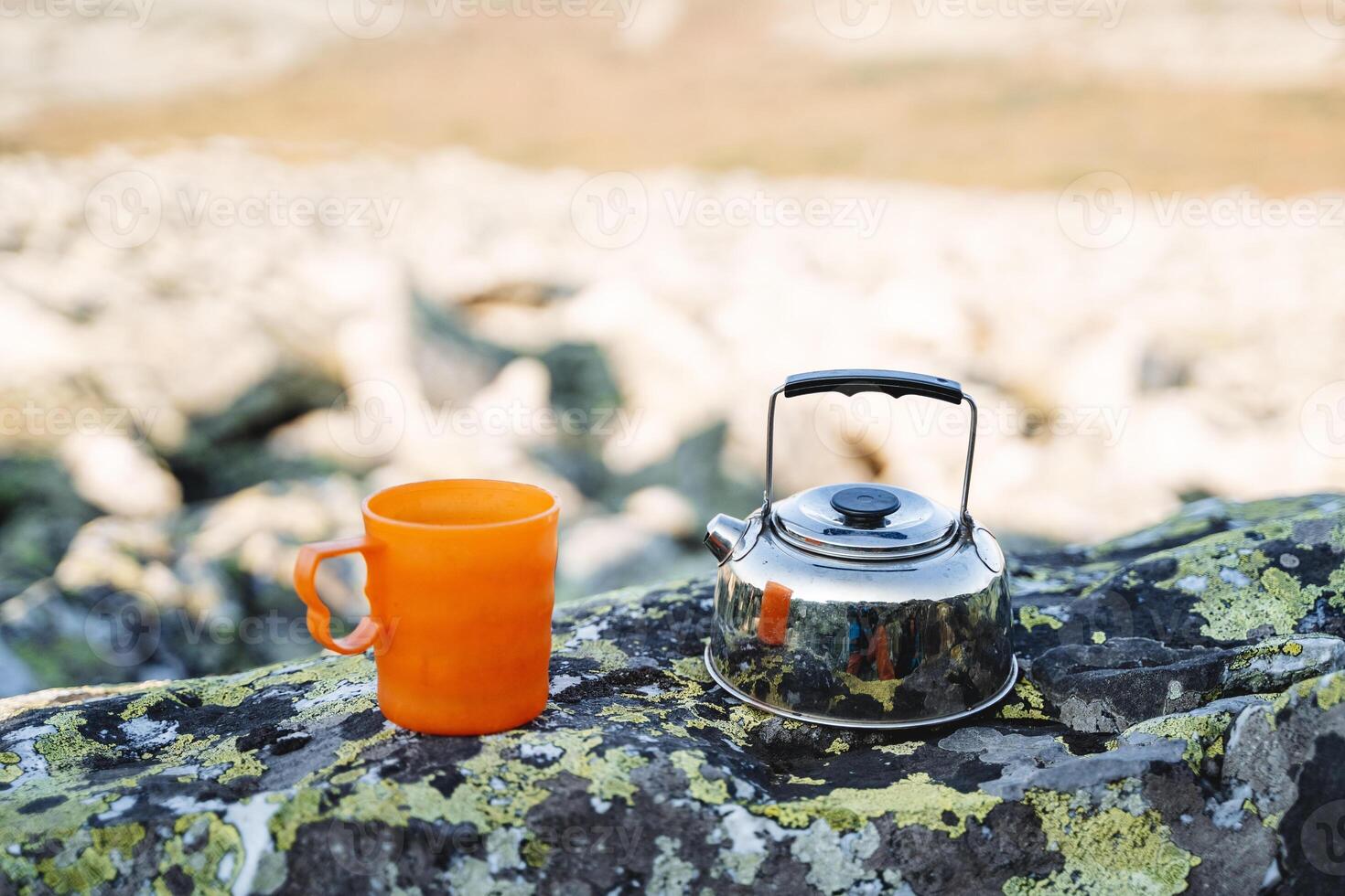 A kettle with a mug stands on a stone on a hike, tourist utensils, a metal kettle, morning coffee, drink tea in the mountains, a kitchen in nature. photo