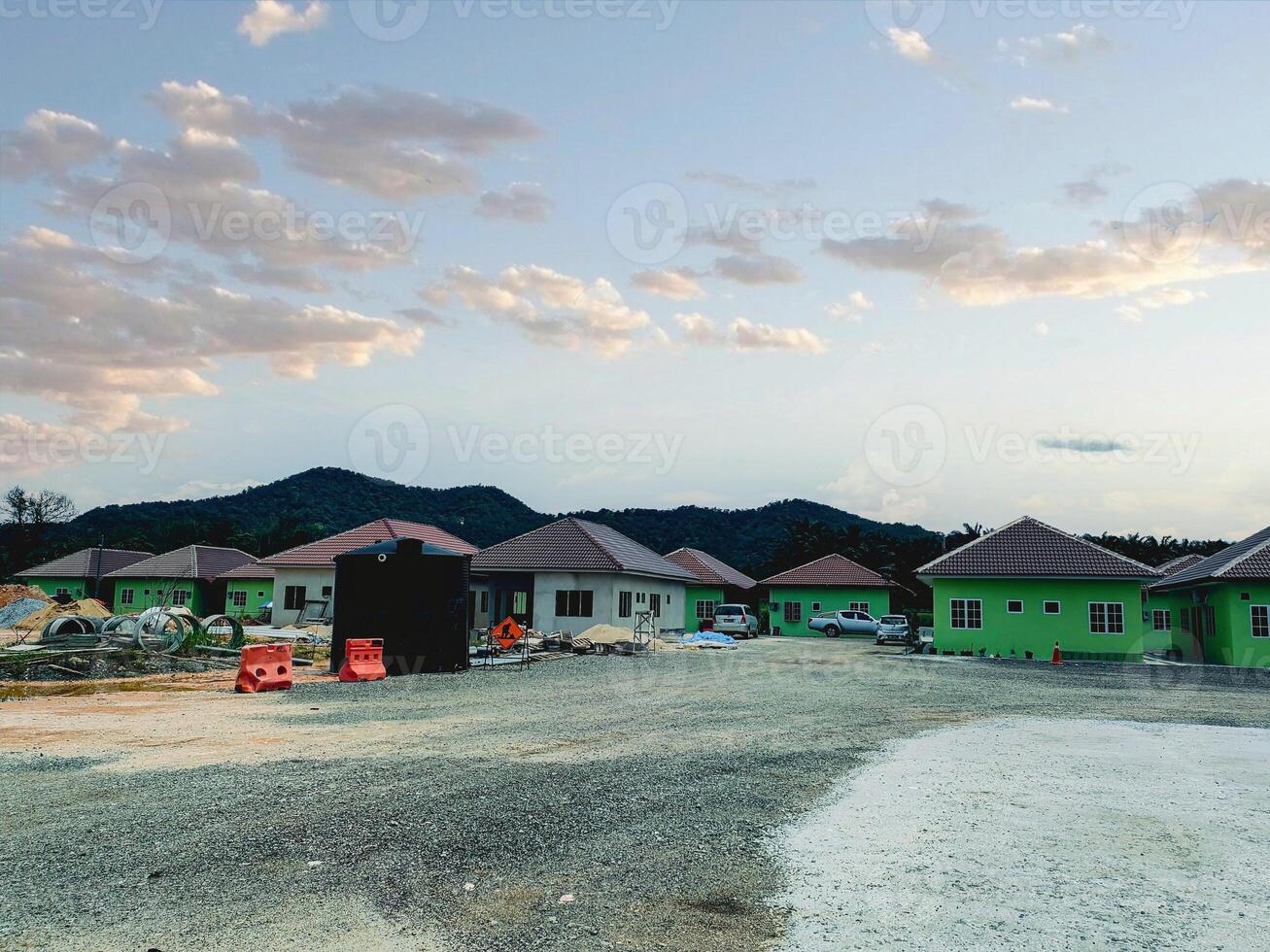 Newly built homes are arranged neatly in a residential development surrounded by mountains in Perak, Malaysia, with construction materials scattered across the site. photo