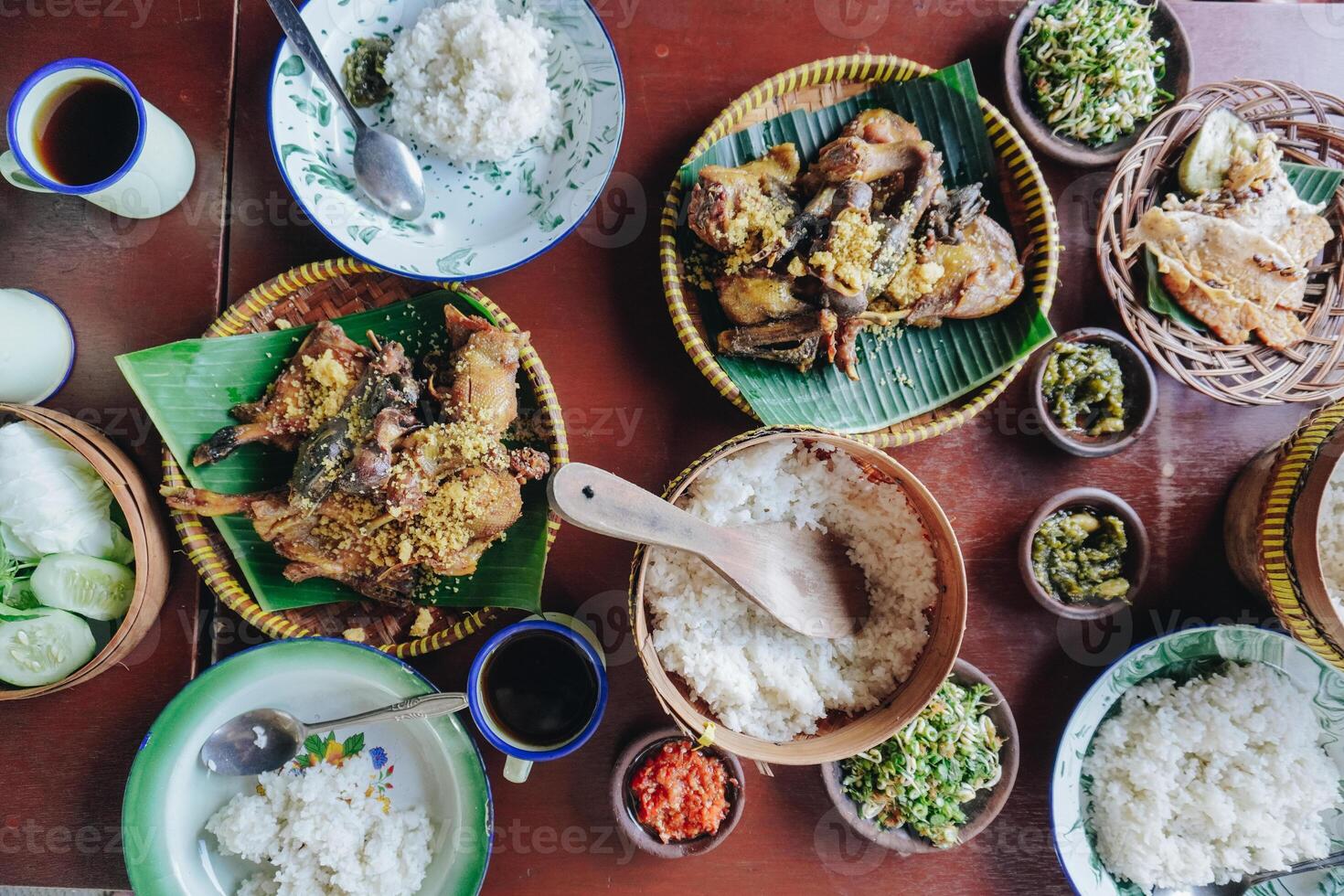 A table with a variety of Asian food, including rice, meat, and vegetables, set with plates, bowls, and utensils. photo