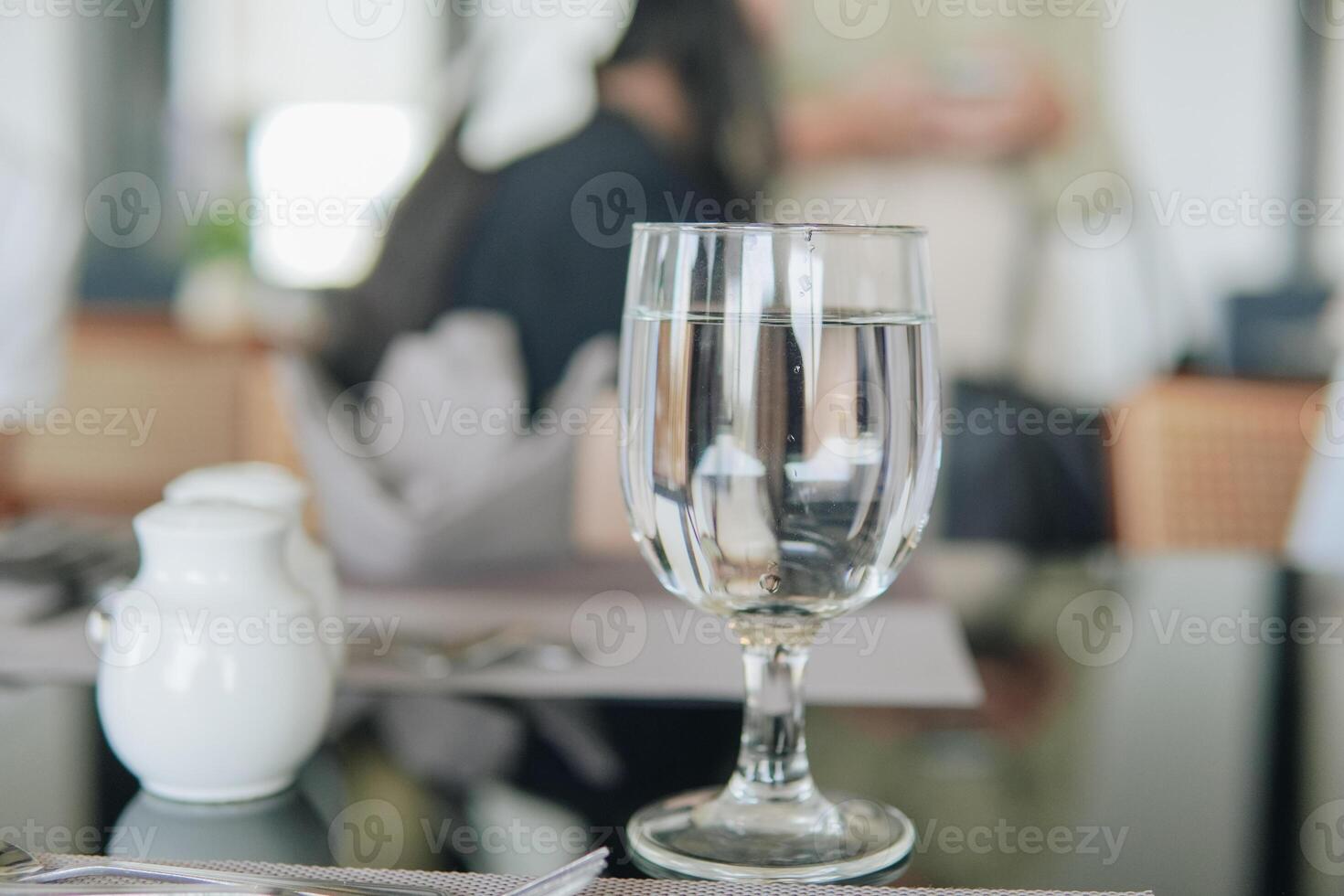 A glass of water sits on a table with a napkin and a salt shaker, set in a restaurant or a cafe. photo