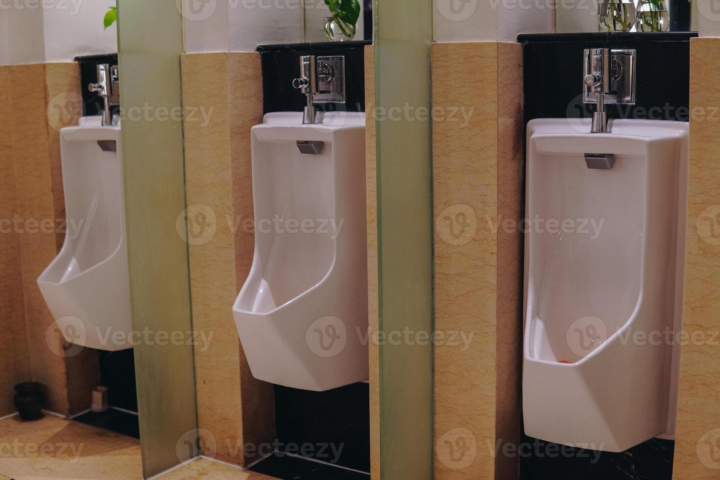 Three white urinals are lined up in a row in a public restroom with a partition between them. photo