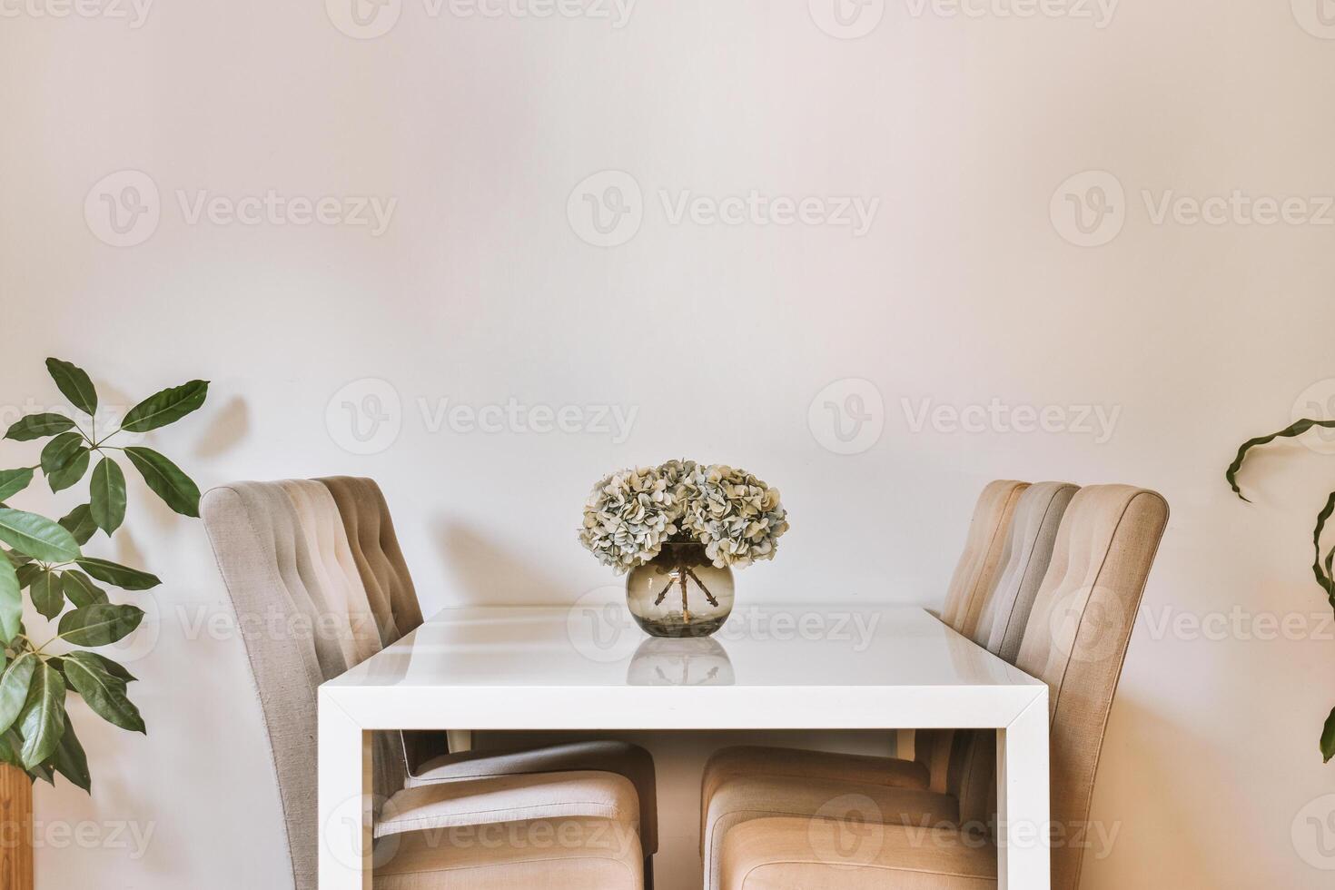 A white dining table with four chairs in front of a plant photo
