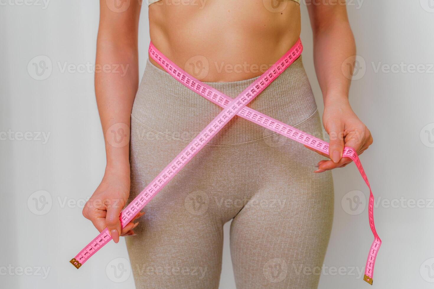 Close up of slim woman measuring her waist's size with tape measure. Isolated on white background. photo