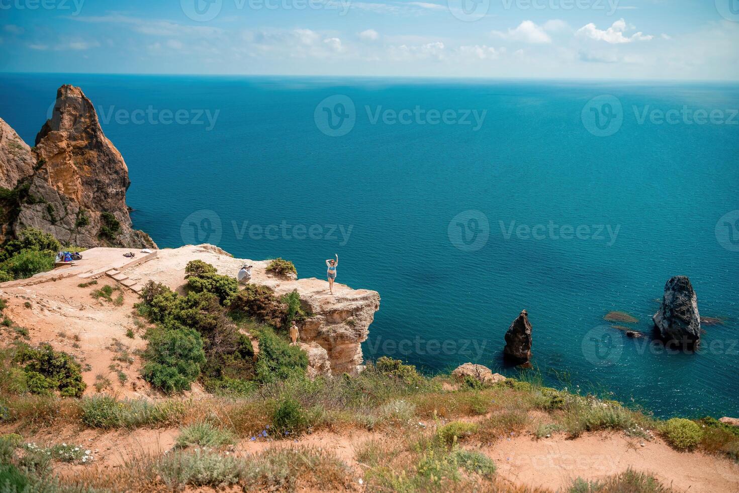 A woman stands on a cliff overlooking the ocean. The water is blue and the sky is clear. photo