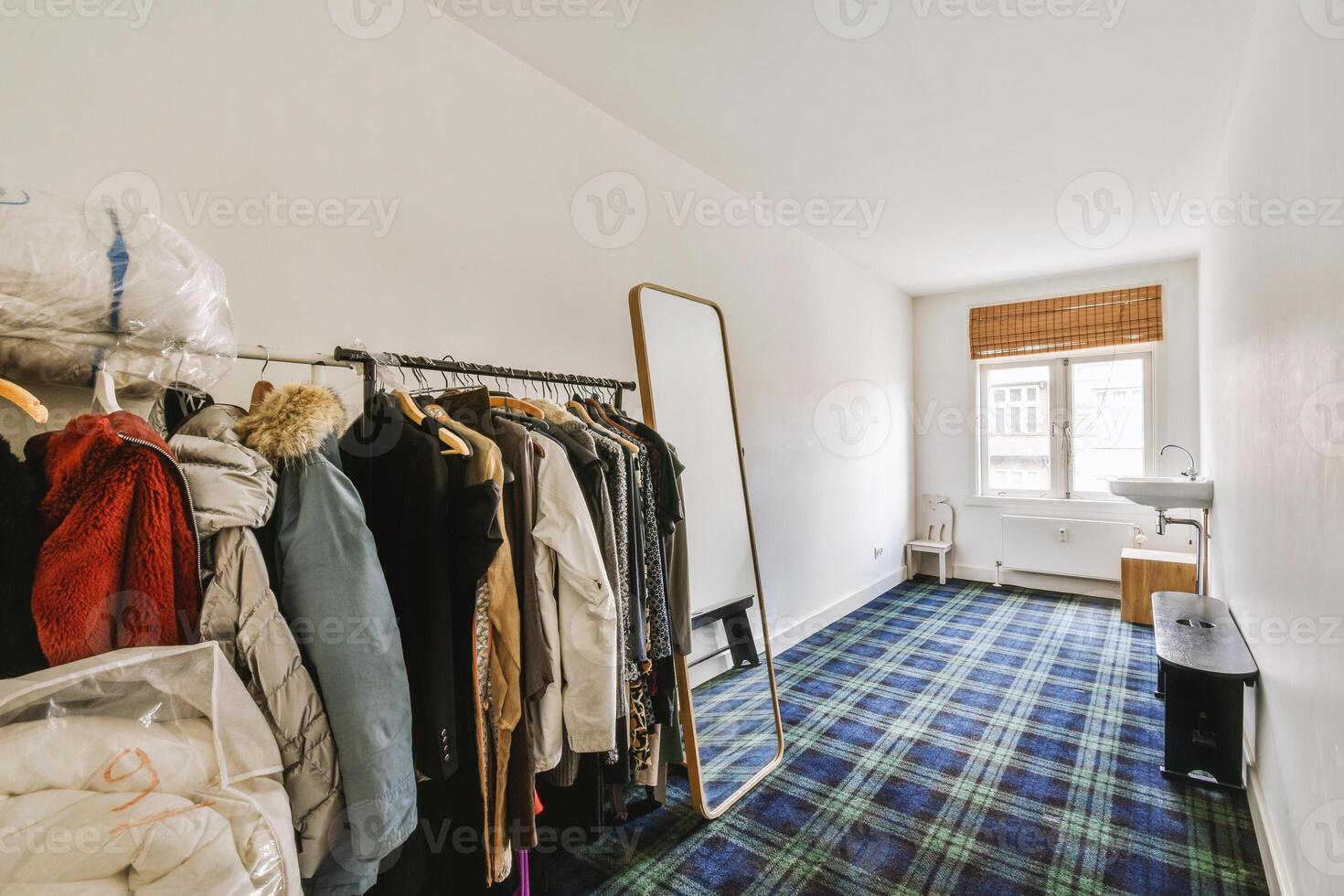 A room with a blue and white plaid carpet and clothes on a rack photo