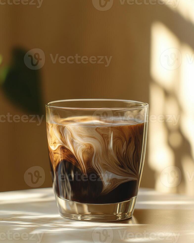 Clear glass cup with dark coffee, light cream swirls forming delicate patterns photo