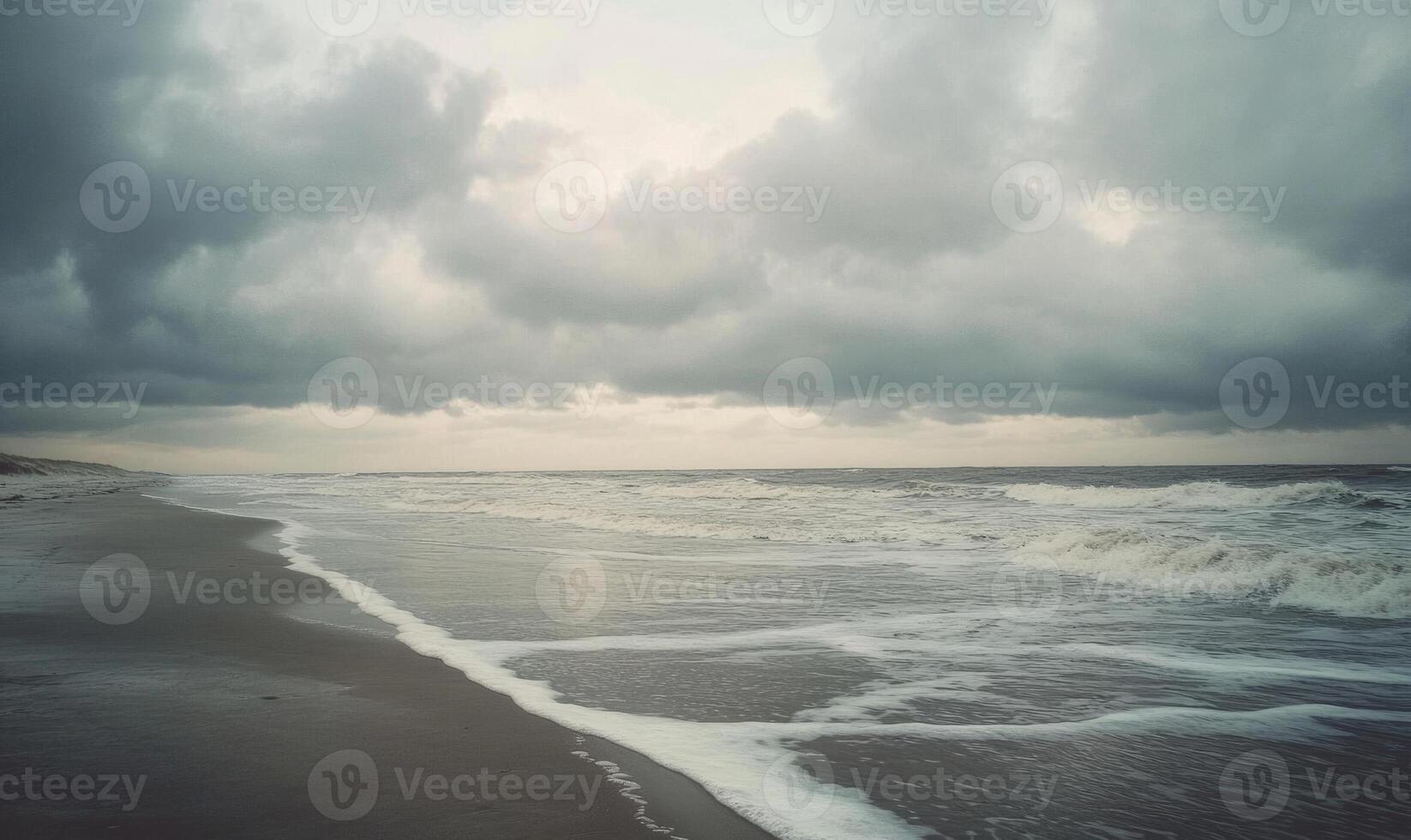Thick, gray clouds moving slowly across the sky, casting shadows over a deserted beach photo