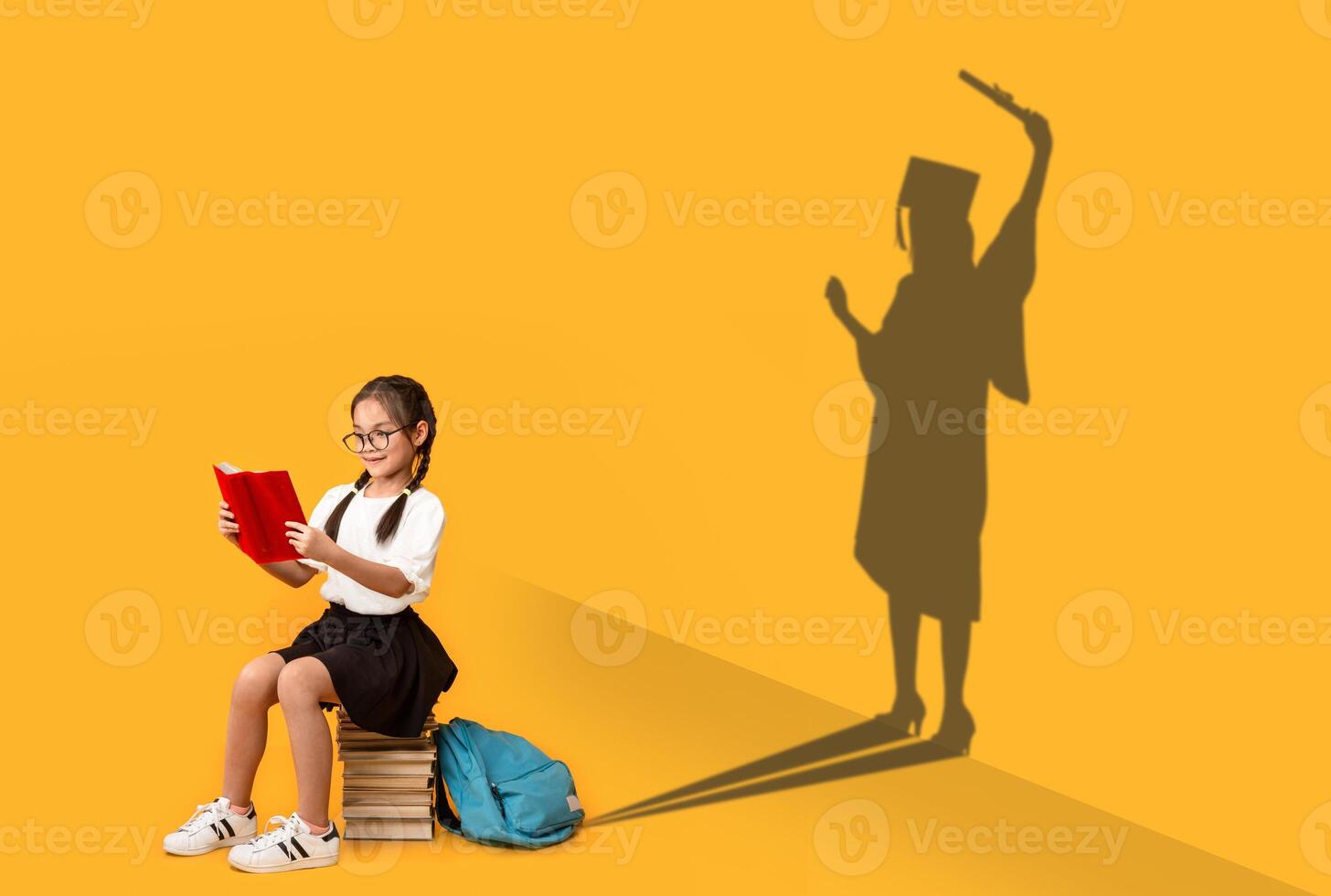 Cheerful Asian Schoolgirl Reading, Sitting On Book Stack, Shape Of Female In Graduation Costume Over Yellow Background, Kid Dreaming About Master Degree, Conceptual Image, Panorama photo