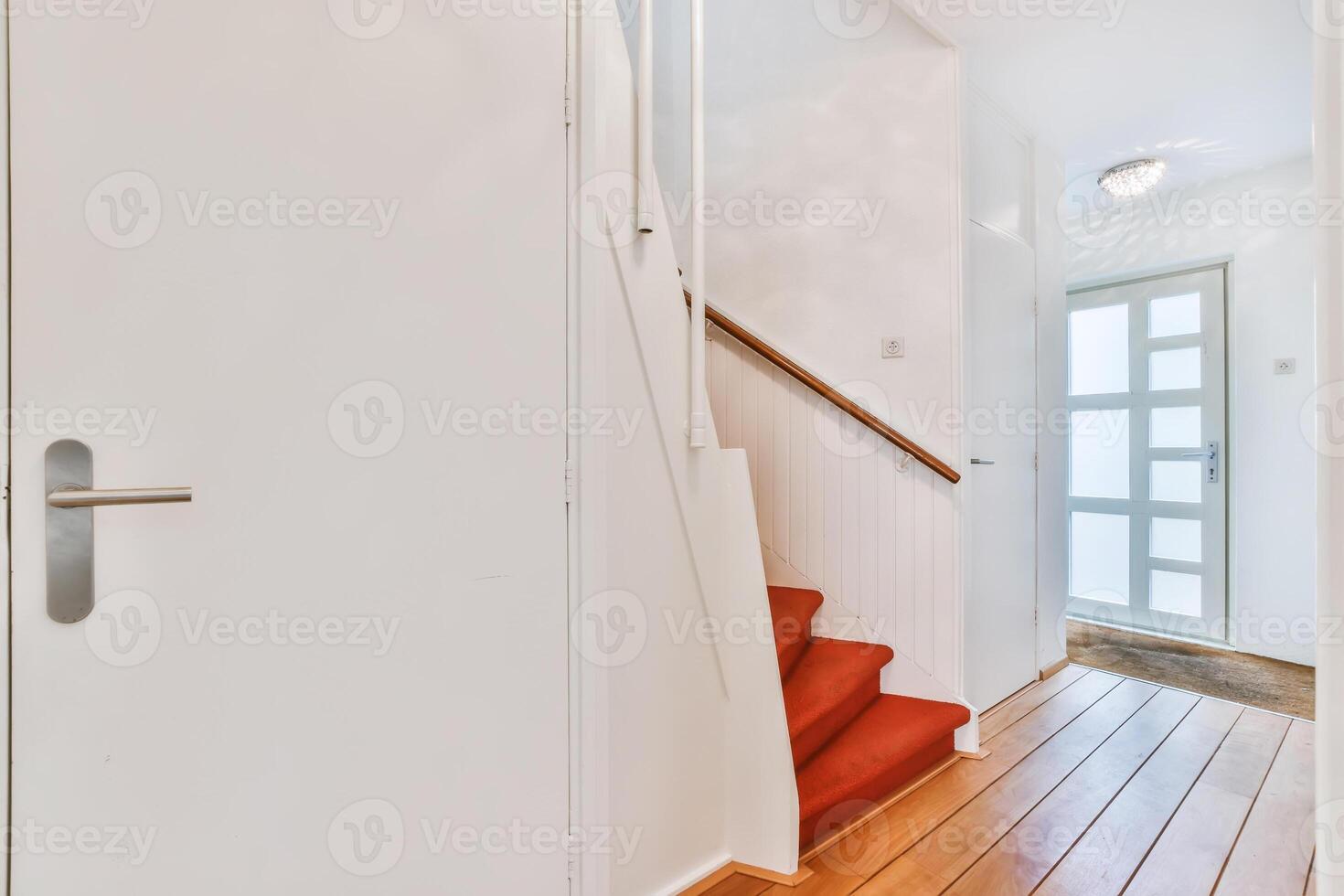 A hallway with a red carpet and wooden stairs photo