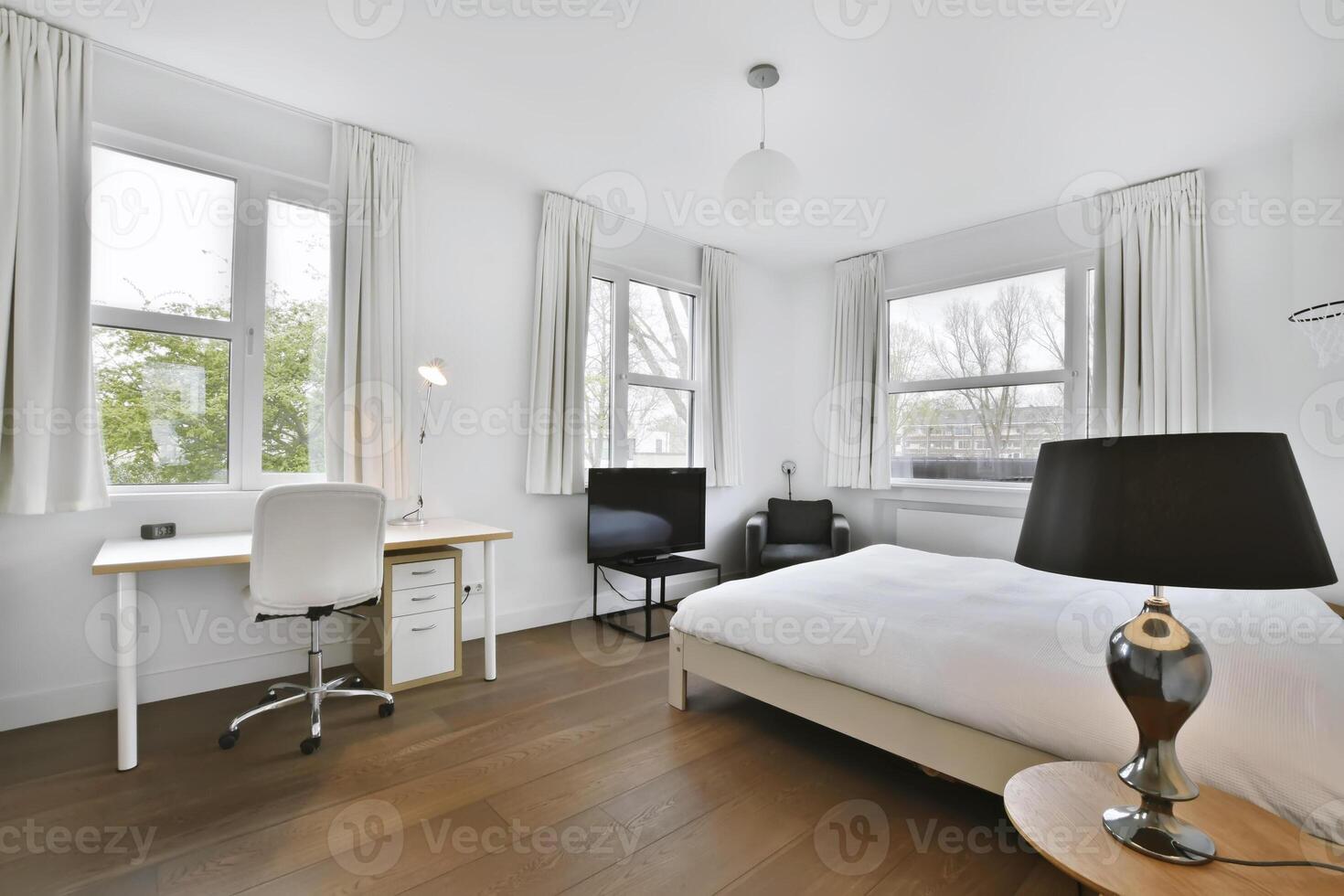 A white bed in a bedroom with a desk and a window photo