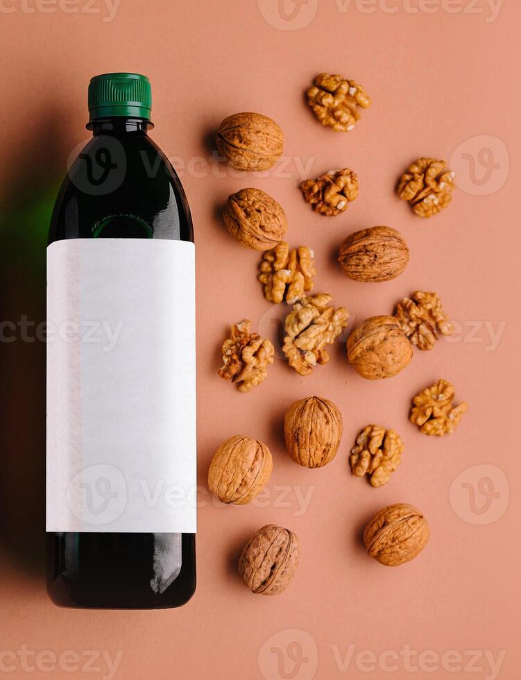 Bottle of walnut oil with walnuts scattered around on orange background photo