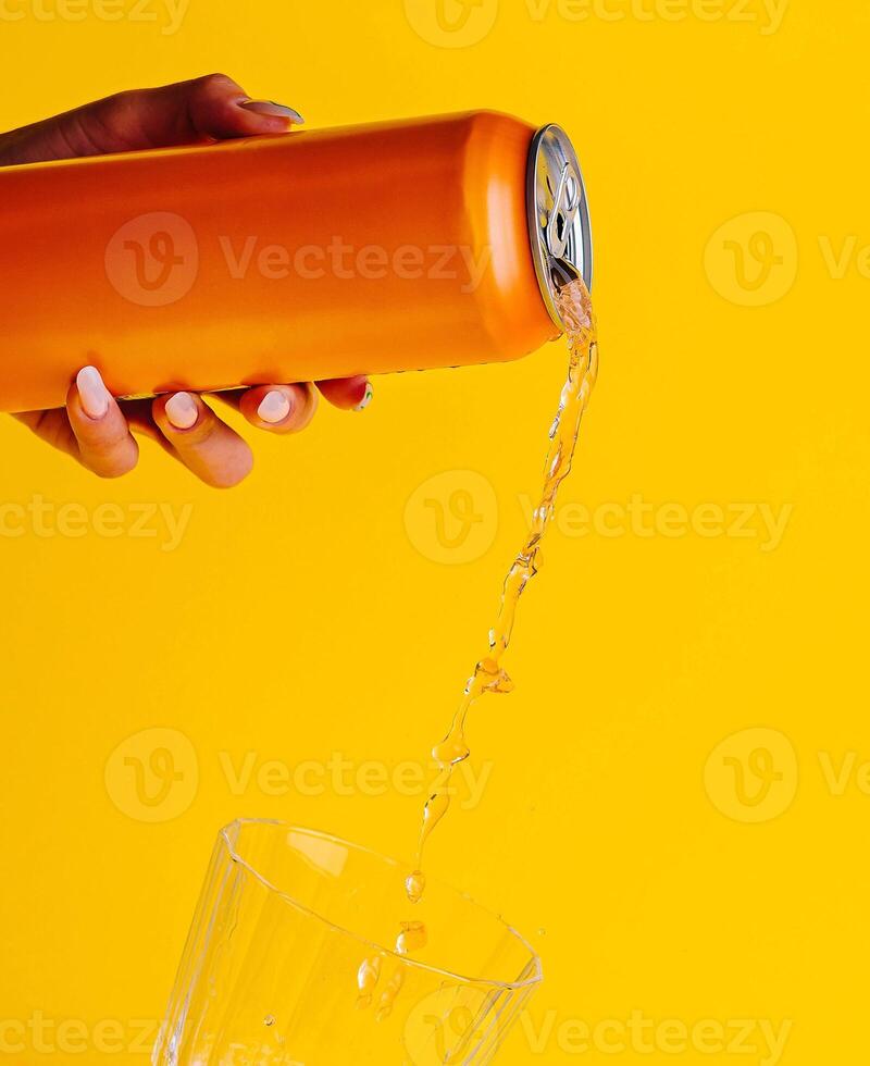 Woman pouring orange juice from can into glass on yellow background photo