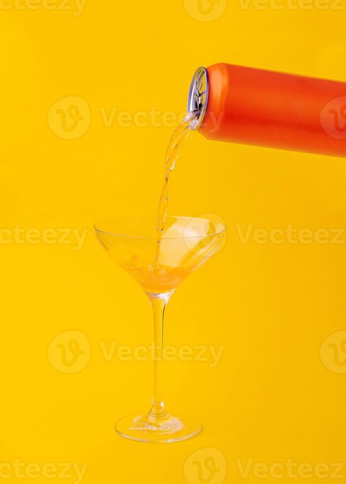 Orange can pouring drink into cocktail glass on yellow background photo