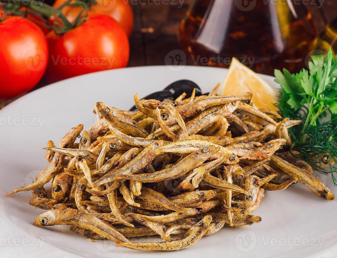 Fried anchovies served on white plate with herbs and spices on rustic wooden table photo