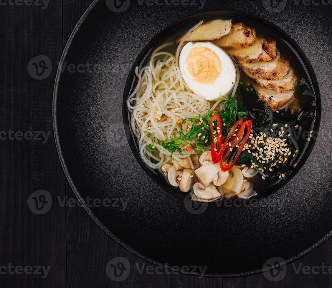 Steaming bowl of chicken ramen on black table setting photo