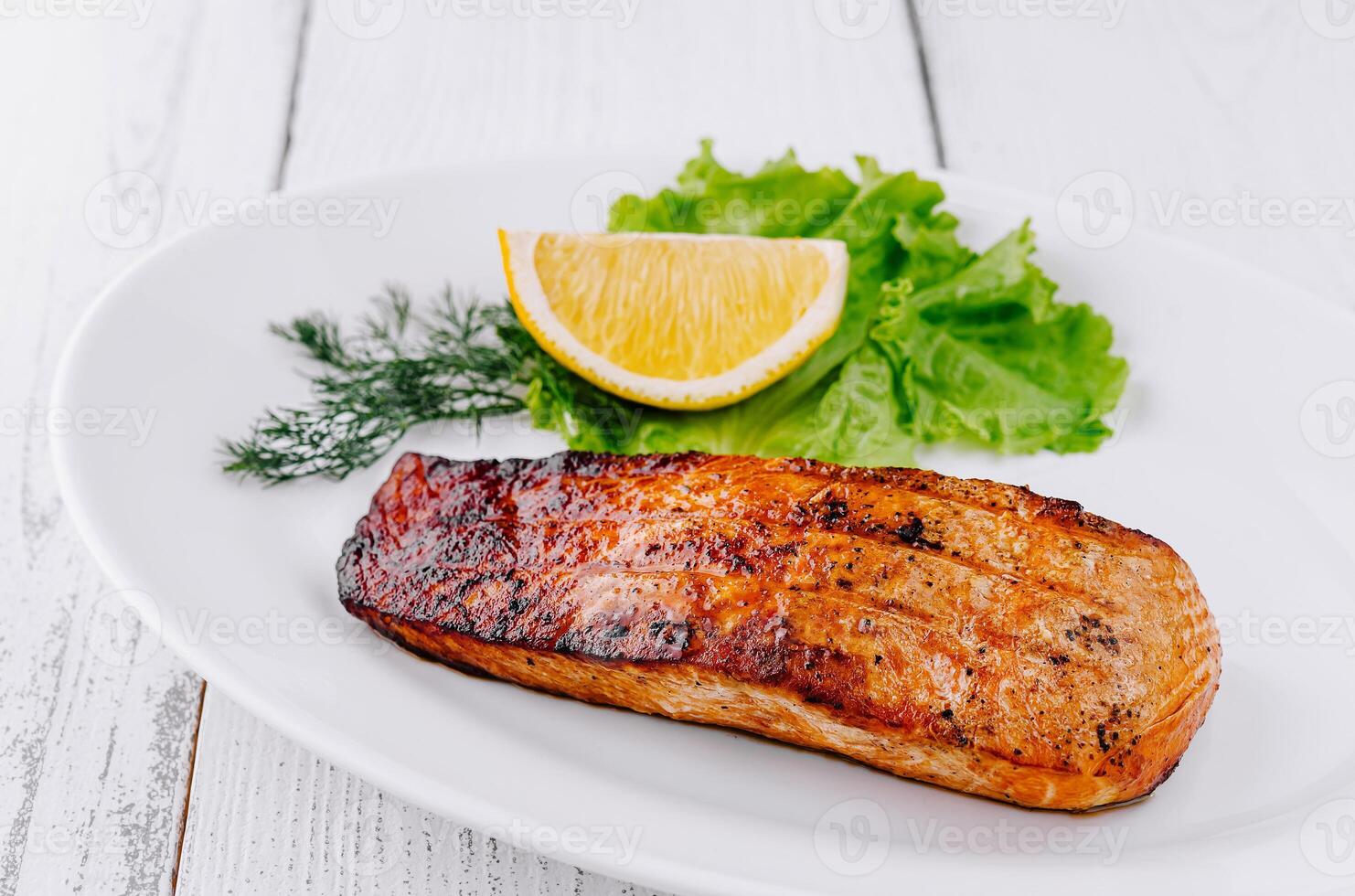 Grilled salmon steak lying on white plate with lemon and lettuce photo