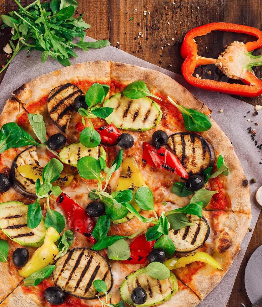 Delicious vegetarian pizza lying on wooden table surrounded by fresh ingredients photo