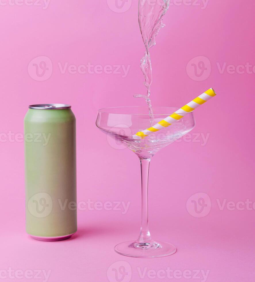 pouring drink from can into glass with straw on pink background photo