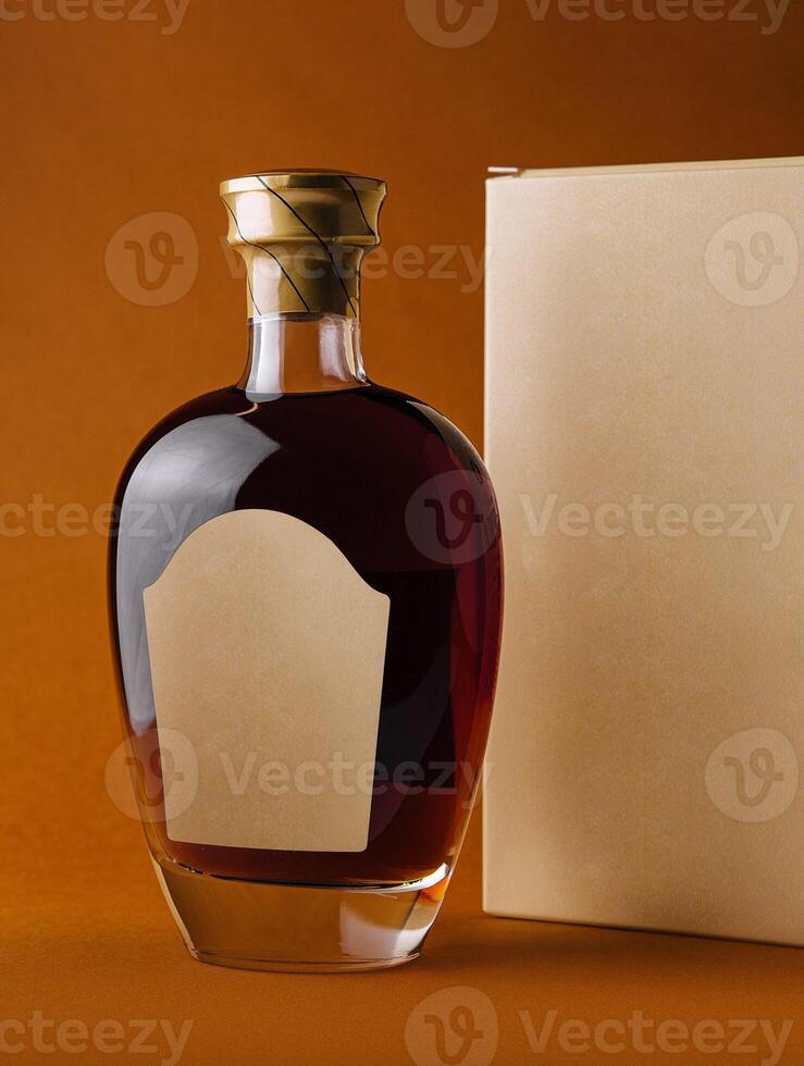 Bottle of alcohol with blank label and cardboard packaging standing on orange background photo