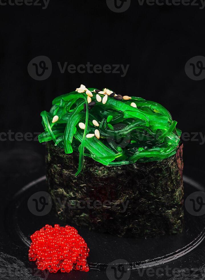 Gunkan maki sushi with chuka seaweed and sesame seeds is served on black stone plate photo