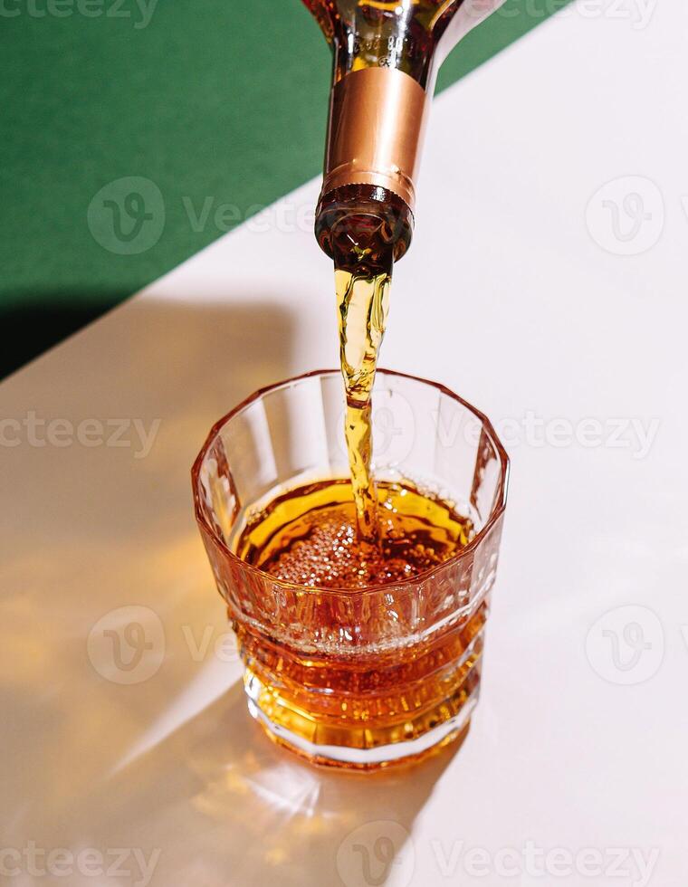 Bartender pouring liquor into crystal tumbler with liquor bottle photo