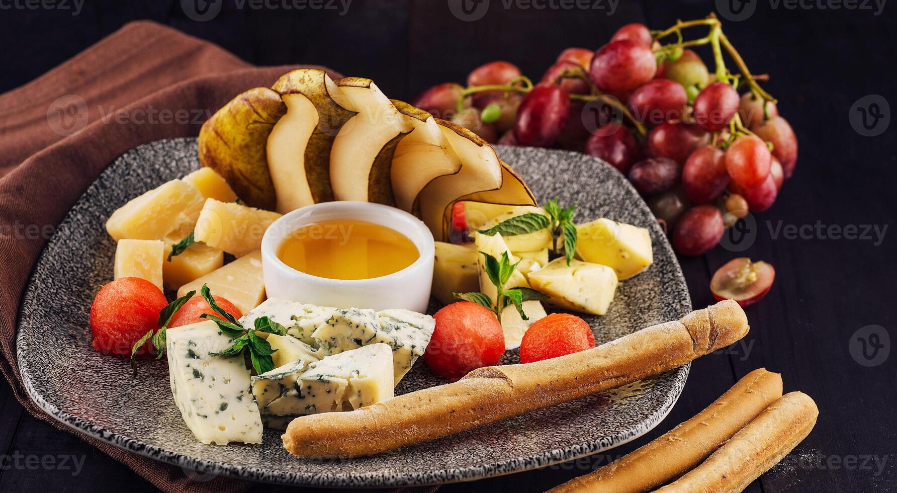 Gourmet cheese plate offering variety of textures and flavors with honey and grapes photo