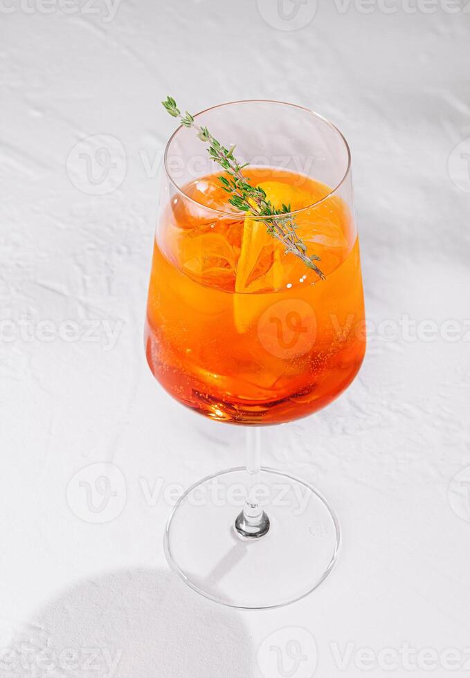 Aperol spritz cocktail standing on white table with thyme garnish photo