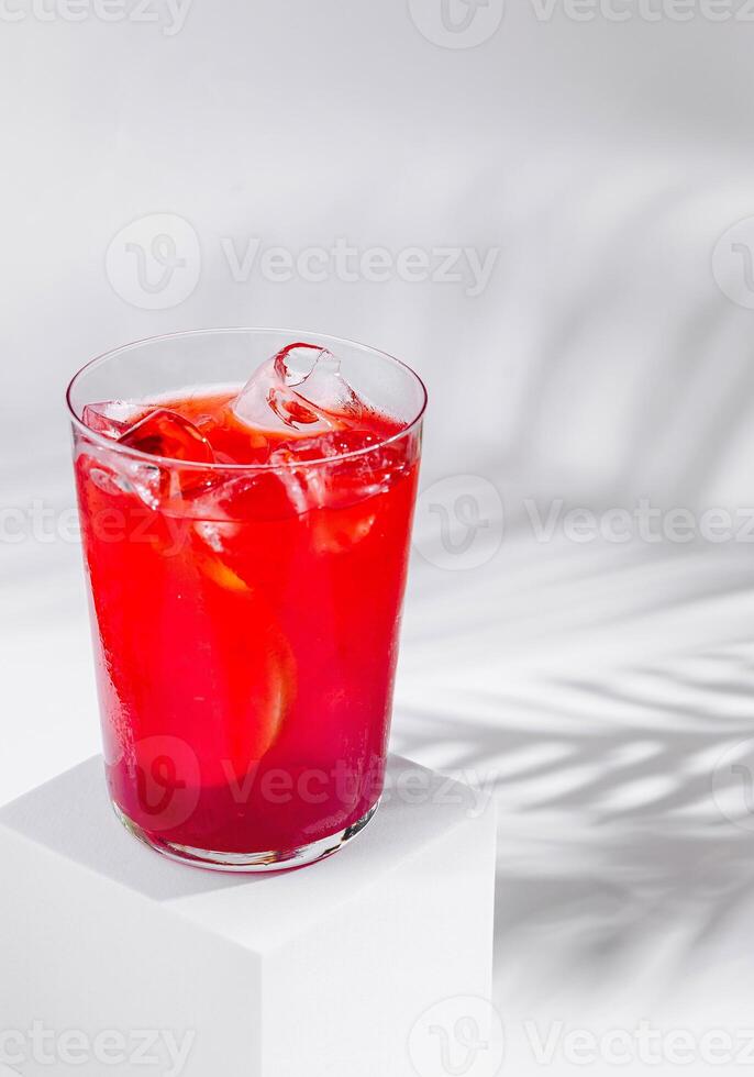 Refreshing red cocktail standing on white cube with tropical palm leaf shadow photo