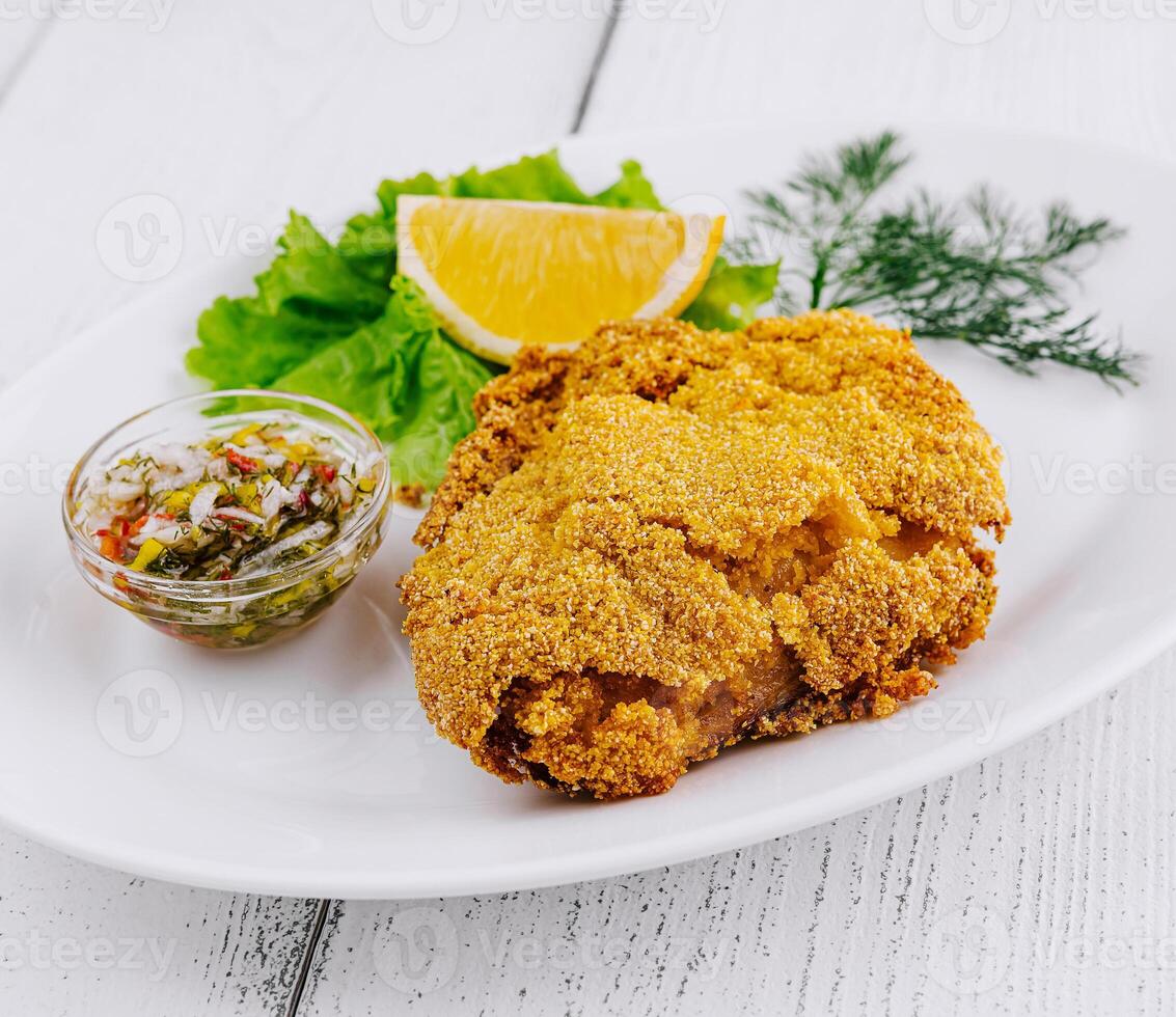 Breaded fish fillet served on white plate with lemon and sauce photo