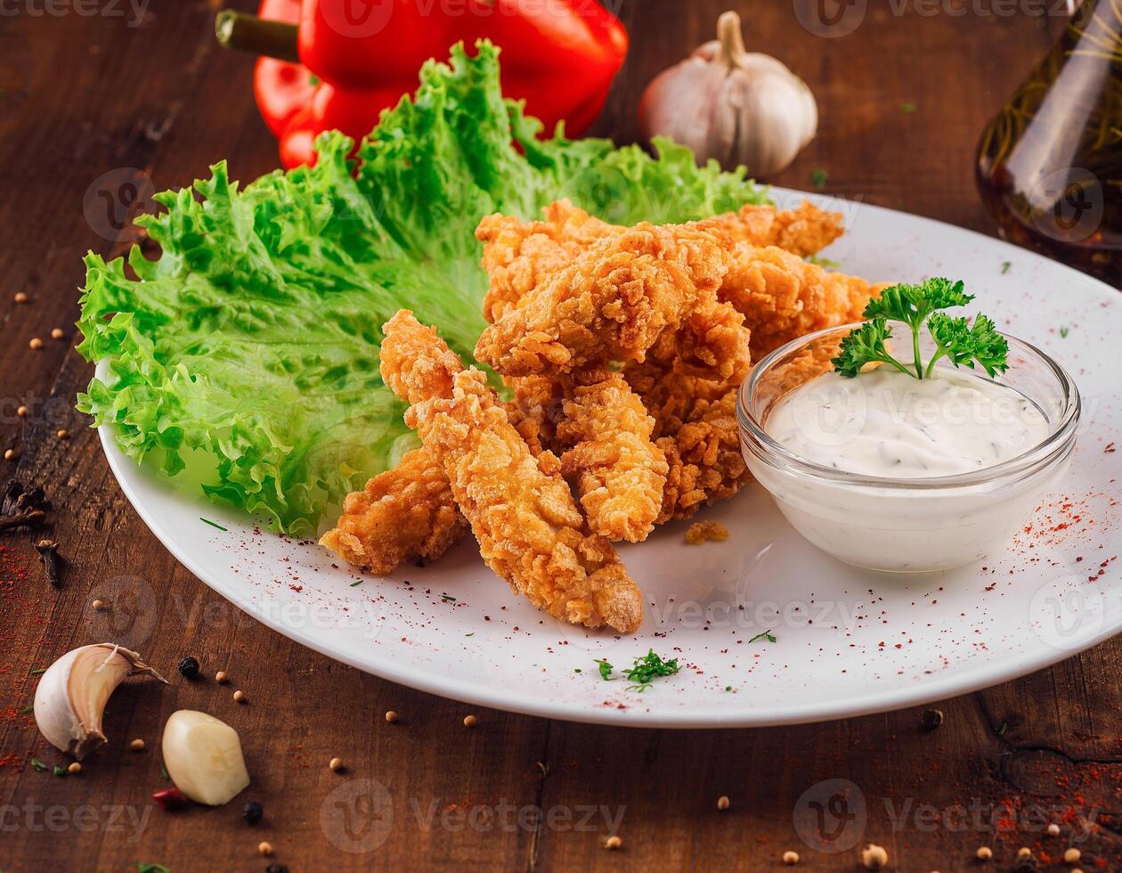 Breaded chicken strips being served on a white plate with dipping sauce photo