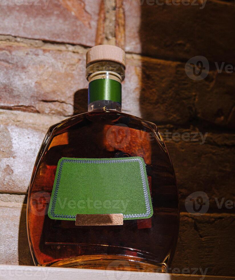Bottle of cognac sitting on shelf with blank label and brick background photo