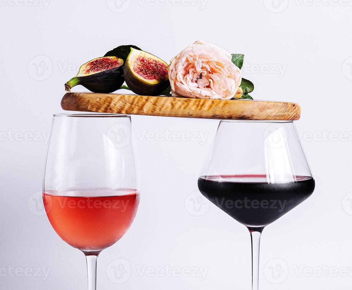 Two glasses with red and rose wine balancing wooden board with ripe figs and pink rose photo