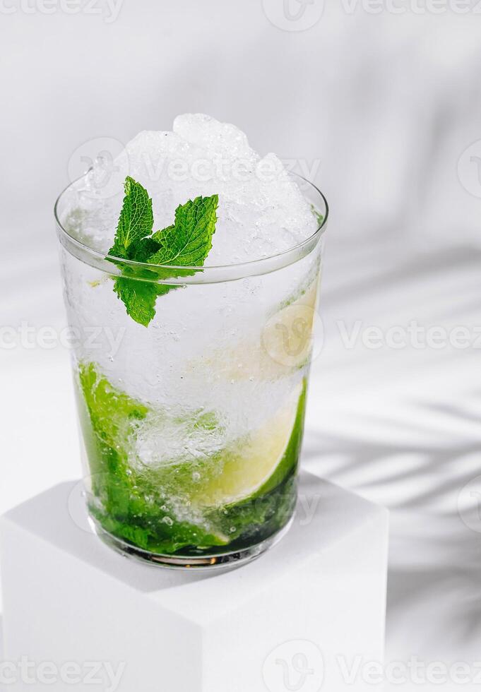 Refreshing mojito cocktail standing on white cube with tropical palm leaf shadow photo