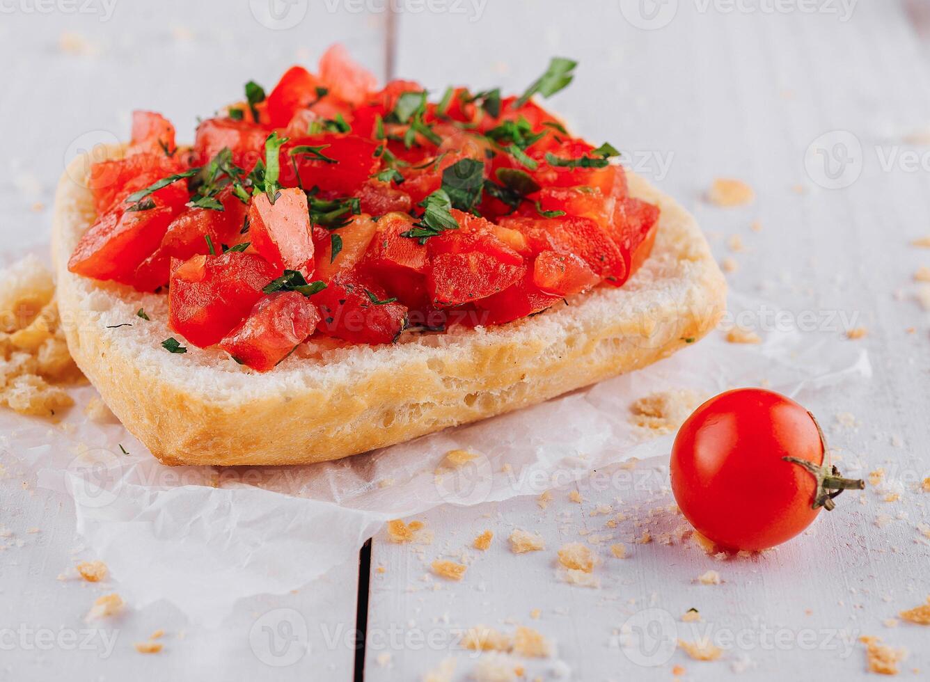 Delicious bruschetta with chopped tomatoes and basil resting on paper on white table photo