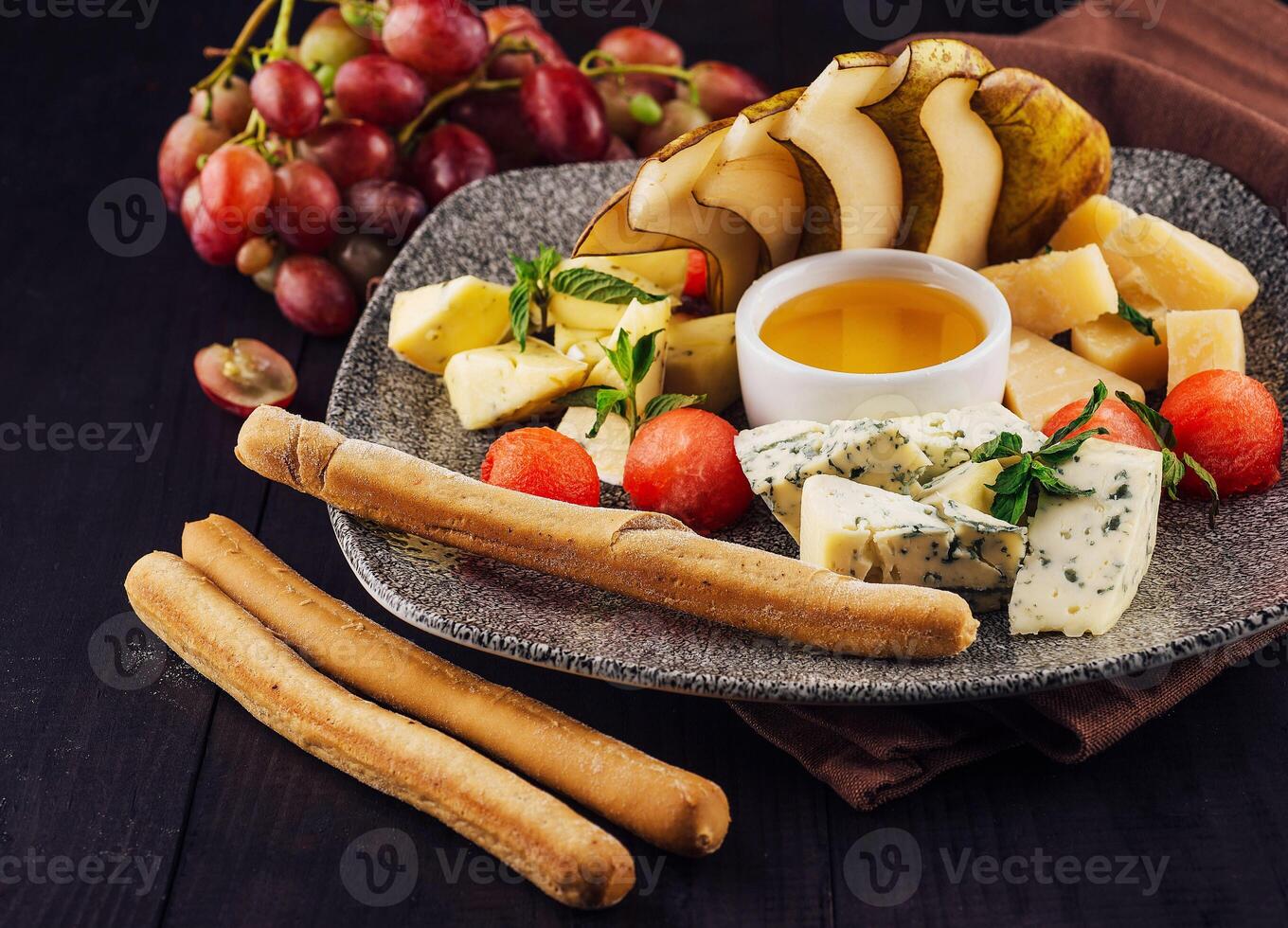 Gourmet cheese plate offering variety of textures and flavors with honey and grapes photo