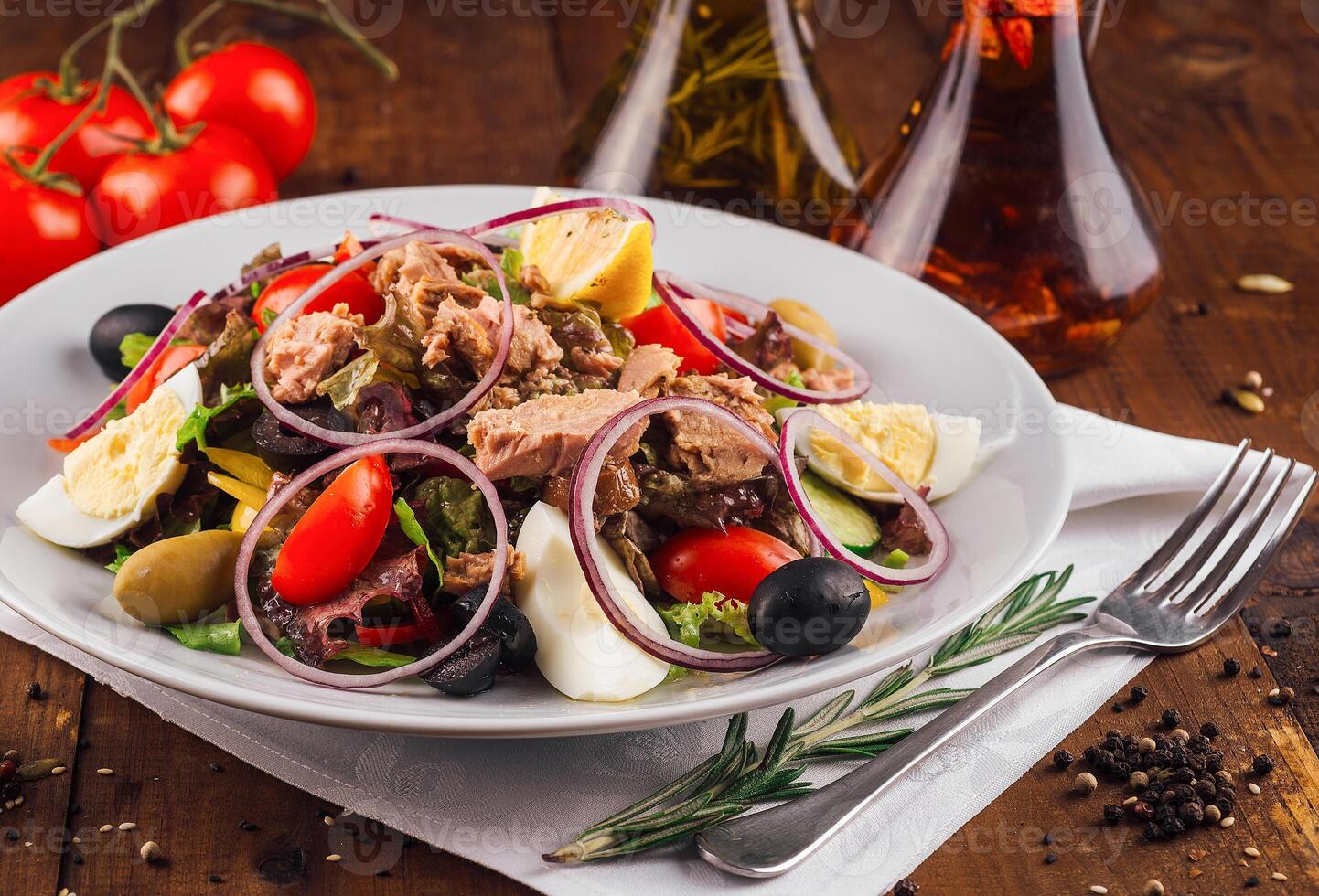 Fresh nicoise salad with tuna on a wooden table being prepared with eggs and tomatoes around photo