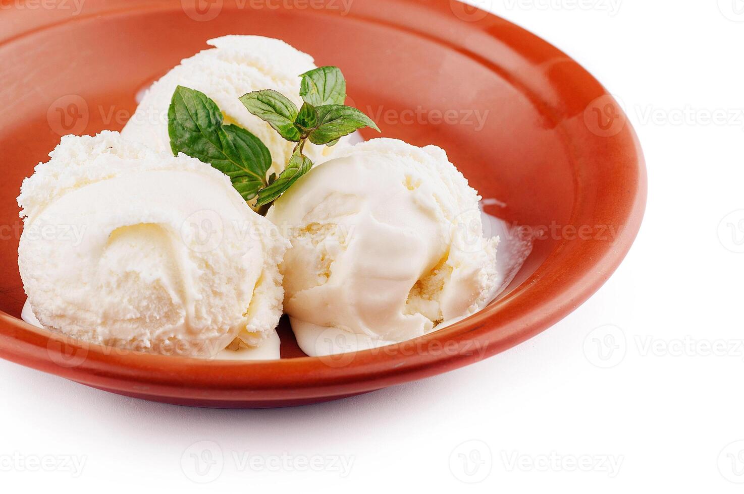Three scoops of vanilla ice cream melting in rustic bowl with mint garnish photo