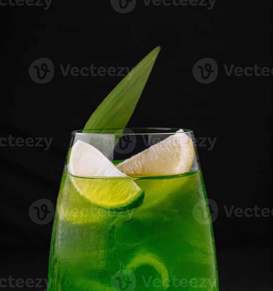 Green cocktail standing on black background with lime and leaf decoration photo