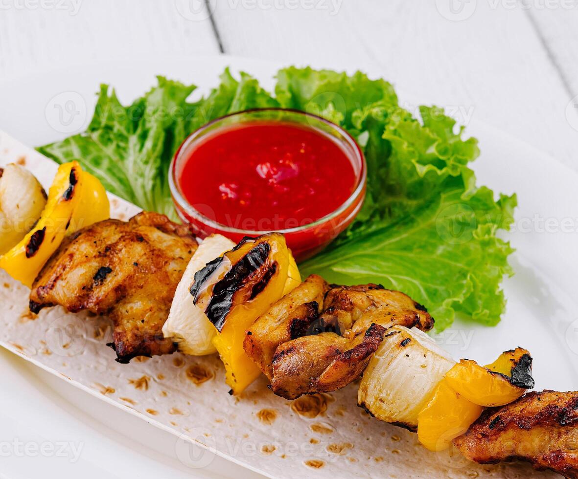 Grilled chicken shish kebab served on pita bread with tomato sauce and lettuce photo