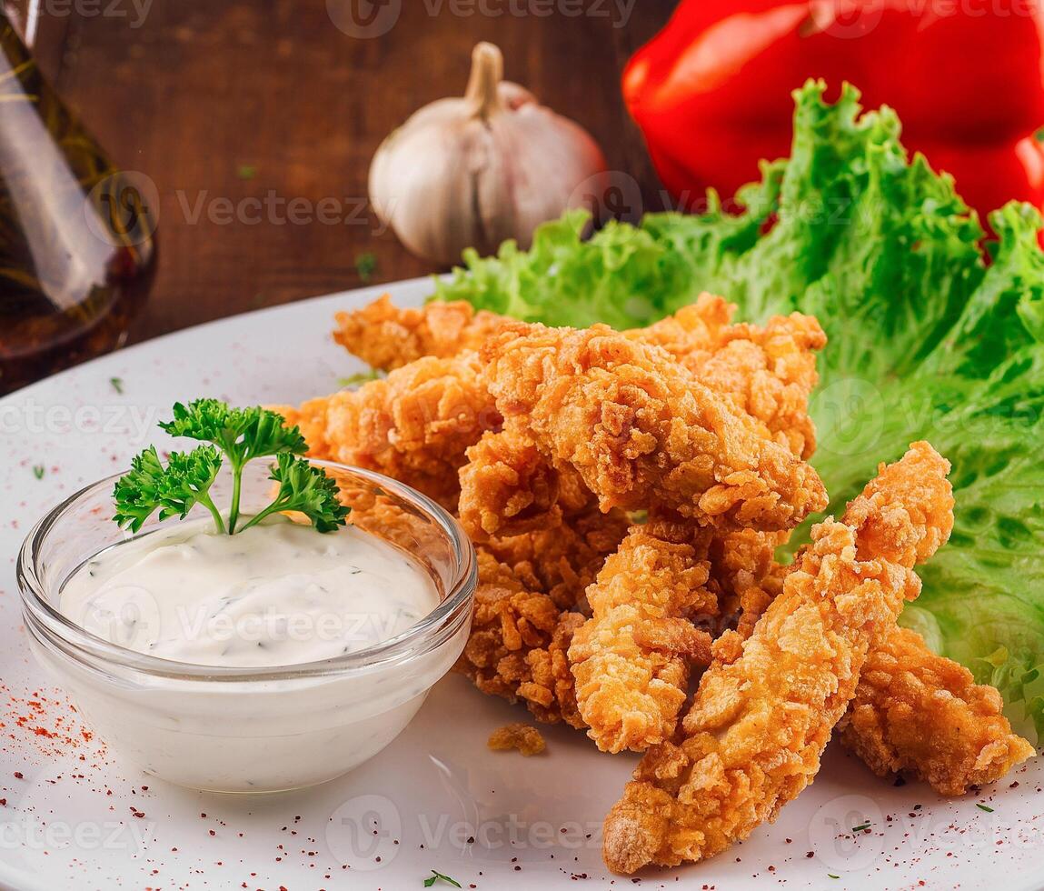 Breaded chicken strips with garlic sauce on a white plate photo