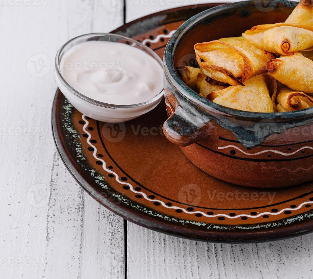 Small baked pies are lying in a ceramic bowl on a white wooden table photo