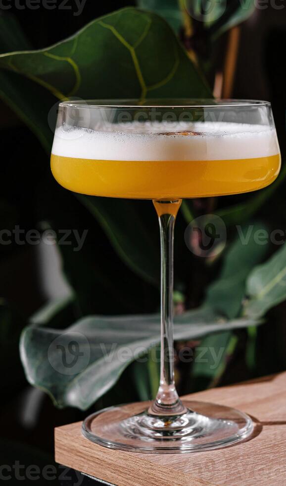 Yellow cocktail standing on bar with tropical plants background photo