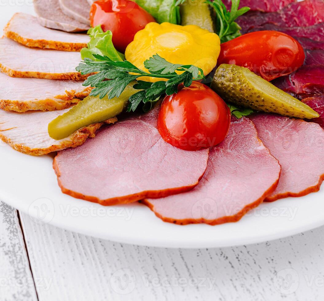 Plate combining several types of meat cuts and pickles being served on white table photo