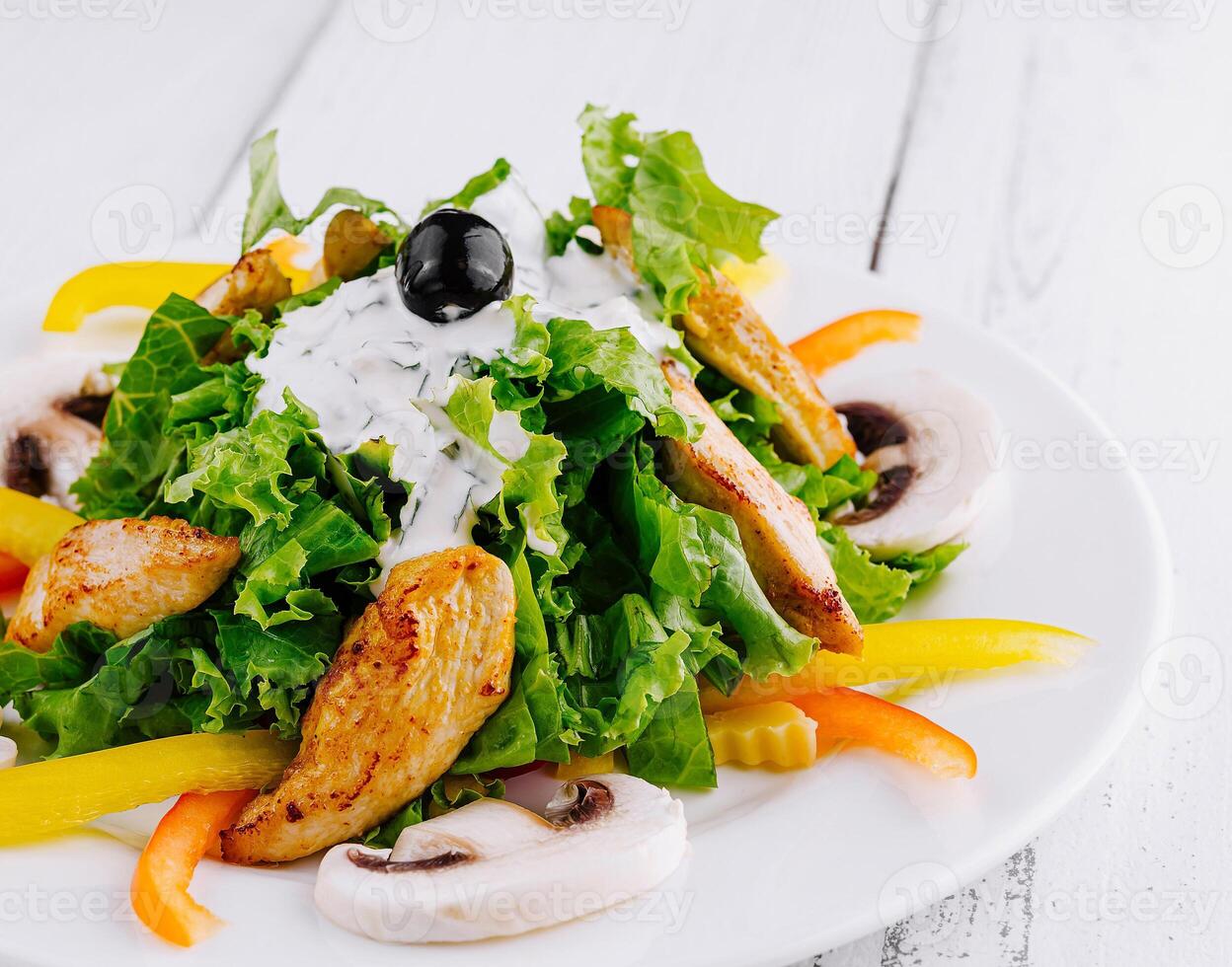 Delicious salad with grilled chicken, mushrooms and yogurt dressing on white wooden table photo