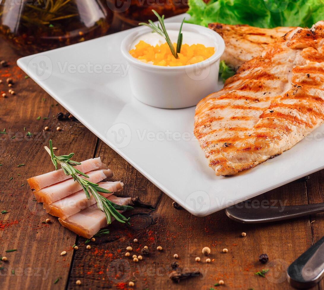 Grilled chicken breast being served on white plate with garnish and sauce photo