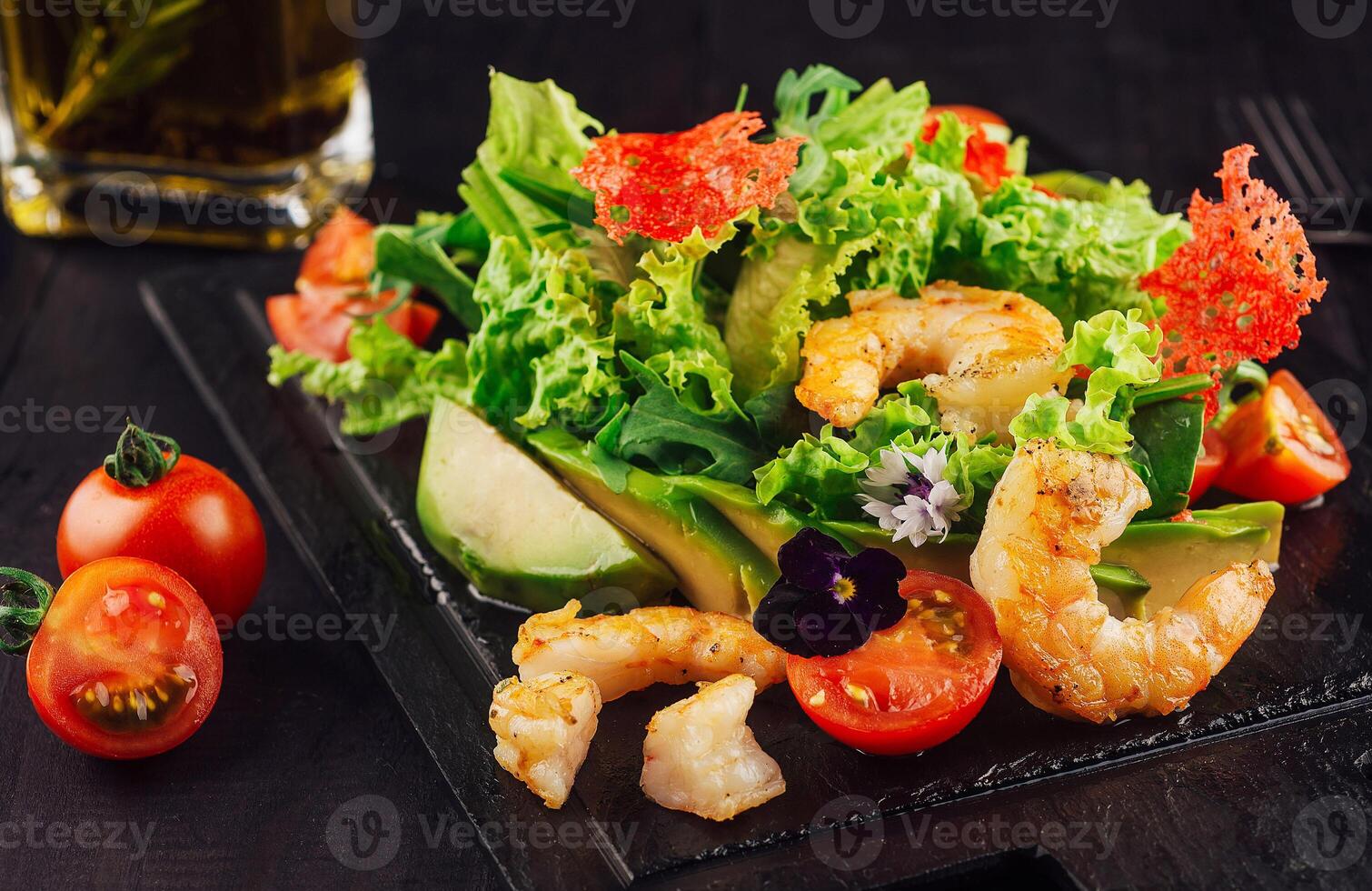 Fresh salad with shrimps, avocado and cherry tomatoes on black wooden table photo