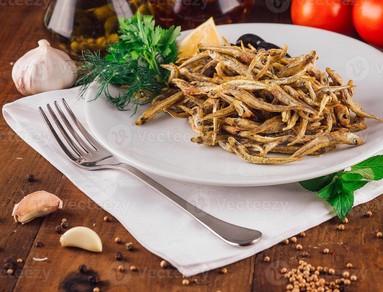 Fried anchovies served on white plate with herbs and spices on rustic wooden table photo