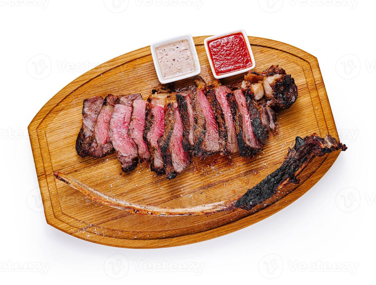 Grilled tomahawk steak lying on wooden board with sauces photo