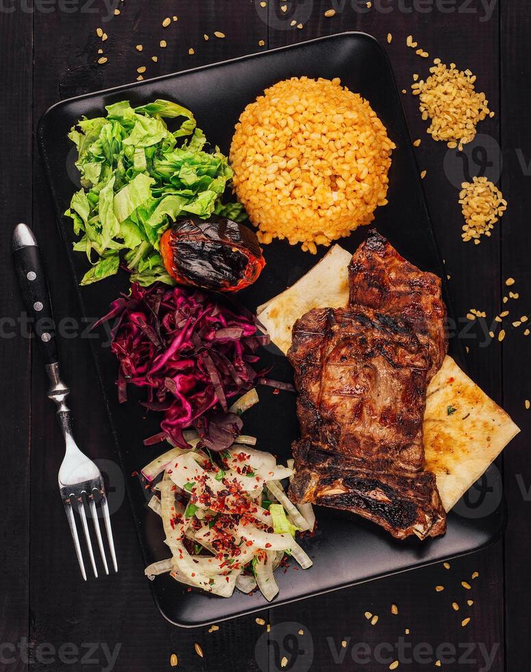 Grilled beef steak served on black plate with bulgur and vegetables photo
